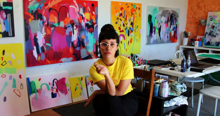 fotografía de la artista Lua Gandara rodeada de sus pinturas